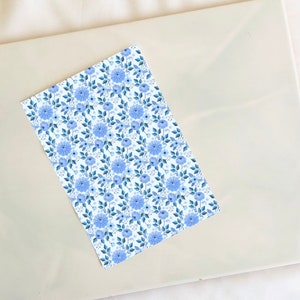 May include: A sheet of white paper with a blue floral pattern. The pattern features small blue flowers and leaves on a white background.