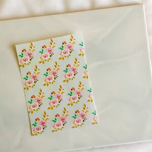 May include: A sheet of white paper with a repeating pattern of pink and orange flowers with green leaves and gold branches.