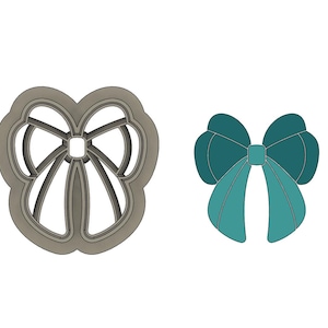 May include: Two cookie cutters in the shape of a bow. The first cutter is a solid gray and the second cutter is a teal blue.