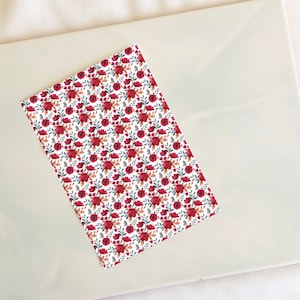 May include: A white sheet of paper with a repeating pattern of red flowers and green leaves.