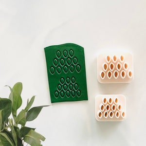 May include: A set of three green and white silicone molds for making fondant or gum paste decorations. The molds feature a honeycomb pattern with small, round indentations.