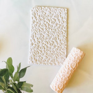 May include: An off-white rectangular stamp and a matching rolling pin, both featuring a repeating pattern of seashells, swirls, and floral designs. The items are displayed on a light background, suggesting a craft or baking theme. The rolling pin is approximately 20 cm long.