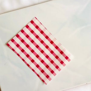 May include: A red and white checkered fabric sheet. The sheet is folded in half and has a smooth texture.