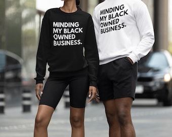 May include: Two people wearing sweatshirts with the text "Minding My Black Owned Business." The person on the left is wearing a black sweatshirt and black shorts. The person on the right is wearing a white sweatshirt and black shorts.