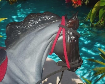 May include: A gray horse figurine with a black mane and a red and black bridle. The text "BRIDLES ONLY NO HORSE" is displayed at the top of the image. The background features a pool of water and colorful flowers.
