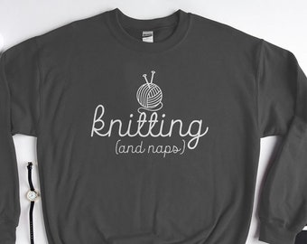 Puede incluir: Una sudadera gris oscuro con el texto "knitting (and naps)" en blanco. Un contorno blanco de una bola de lana con agujas de tejer está por encima del texto.