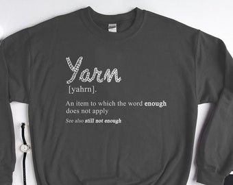 May include: A dark gray sweatshirt with a white graphic that says "Yarn [yahrn]. An item to which the word enough does not apply. See also still not enough."