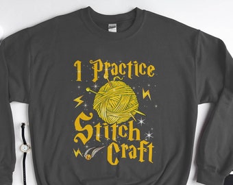 Puede incluir: Una sudadera gris oscura con un gráfico amarillo que dice "I Practice Stitch Craft". El gráfico presenta una bola de hilo con agujas de tejer y un rayo.
