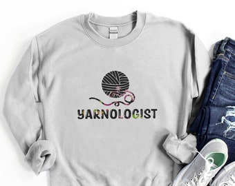 Puede incluir: Una sudadera gris con un gráfico de ovillo de lana en blanco y negro y el texto "YARNOLOGIST" impreso en la parte delantera.