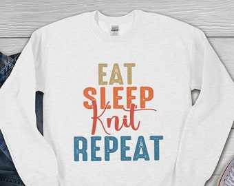 Puede incluir: Sudadera blanca de manga larga con un gráfico de estilo vintage que dice "Eat Sleep Knit Repeat".