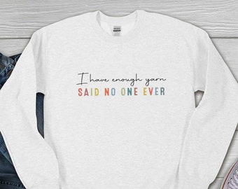 May include: White long-sleeved sweatshirt with the text "I have enough yarn SAID NO ONE EVER" in black with rainbow colored letters.