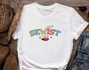 Könnte beinhalten: Weißes T-Shirt mit dem Text "SEWIST" in bunten Buchstaben, einem Herzen und einem roten Nadelkissen.