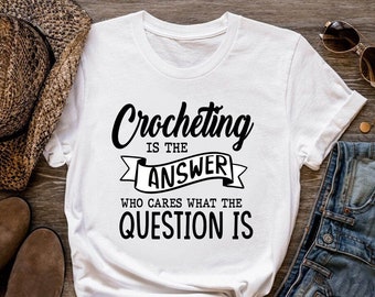 May include: White t-shirt with black text that reads "Crocheting is the answer. Who cares what the question is."