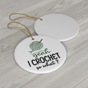 Könnte beinhalten: Weißer Keramik-Anhänger mit einer grünen Wollkugel und einer Häkelnadel und dem Text "yeah I CROCHET so what?"