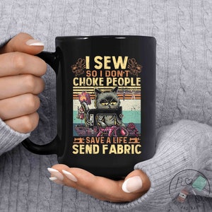 May include: Black coffee mug with a vintage-style graphic of a cat sewing on a sewing machine. The text reads "I sew so I don't choke people save a life send fabric".