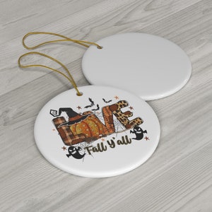 Può includere: Ciondolo rotondo in ceramica bianca. Il ciondolo presenta una grafica della parola "LOVE" con una zucca, un cappello da strega e pipistrelli. Il testo "Fall y'all" è sotto la grafica.
