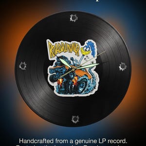 May include: Black vinyl record clock featuring a Roadrunner cartoon design. The clock has a black face with silver hands and bullet hole accents. Text on the clock reads "The Ultimate MOPAR Timepiece."