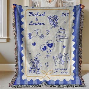 May include: A woven throw blanket with a blue and cream design. The blanket features a blue border and a cream-coloured centre with blue illustrations of wedding-related elements, including a cake, balloons, and the date October 6th, 2025.