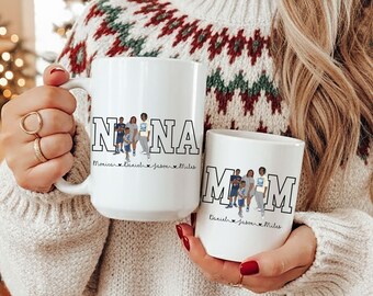 May include: Two white ceramic mugs, one large and one small, featuring custom family illustrations. The large mug says "NINA" and the small mug says "MOM". Both mugs have family member names below the illustrations.