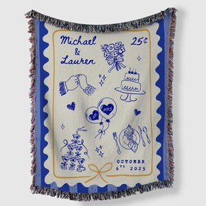 May include: A woven throw blanket with a blue border and fringe. The cream-coloured centre features blue line art of wedding-themed illustrations, including a cake, flowers, and balloons. Text includes names and a date.
