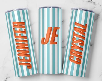 May include: Three personalized skinny tumblers with a vertical striped pattern in light blue and white. The names "JENNIFER", "JE", and "CRYSTAL" are displayed in orange, 3D-style lettering. The tumblers are cylindrical and have a silver lid.