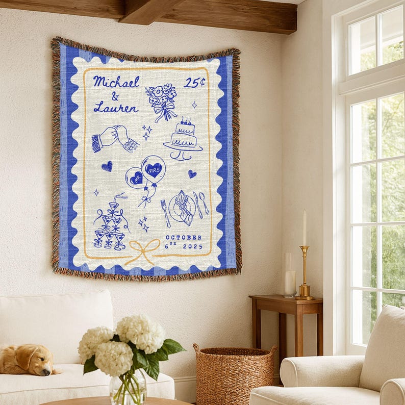 May include: A cream-coloured throw blanket with a blue postage stamp design. The design features the names "Michael & Lauren", illustrations of a bouquet, cake, and balloons, and the date "October 6th 2025".