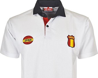 Pode incluir: Camisola polo branca de manga curta com gola preta e vermelha. A camisa tem um botão vermelho e dois logotipos bordados: uma bola de futebol com a palavra "SPAIN" e um escudo com a palavra "SPAIN" e a bandeira espanhola.