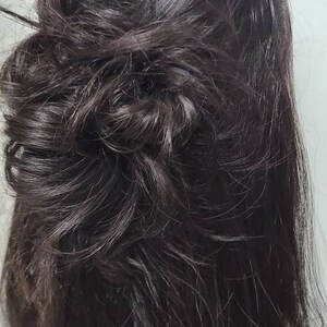 Op de afbeelding: Donkerbruin haar gestyled in een lage, rommelige knot. Het haar is lang, met losse lokken die het gezicht omlijsten. De knot is getextureerd en volumineus, waardoor een casual, maar elegante look ontstaat.