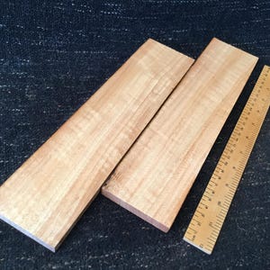 May include: Two light-colored wooden boards and a wooden ruler with inch markings. The boards have a natural wood grain pattern. The ruler is placed next to the boards, showing measurements.