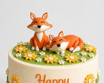 May include: A round cake with smooth off-white frosting, decorated with orange and white fondant fox figures on top. The top features a green fondant base with yellow and white flowers. The side displays orange text reading Happy Birthday.