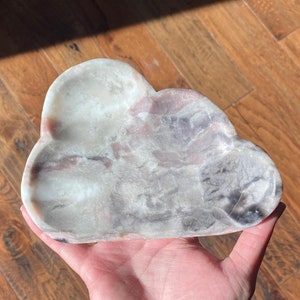 May include: A white, pink, and grey cloud-shaped dish made of natural stone. The dish is carved to resemble a cloud and has a smooth, polished surface.