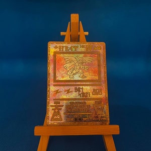 以下が含まれることがあります： 雷のシンボルを持つドラゴンに似た生き物を描いた、金色のホログラフィックポケモンカード。カードは木製イーゼルの上に置かれています。