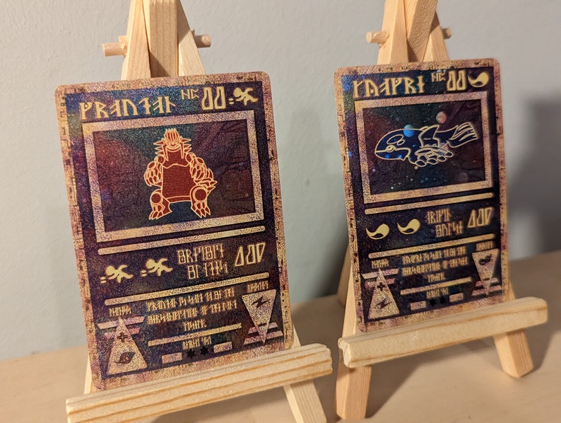 May include: Two vintage-style trading cards with holographic foil accents. The card on the left features a red monster with the text "PRANIAL NO. 00-.", while the card on the right features a blue creature with the text "MAPRI NO. 00-."