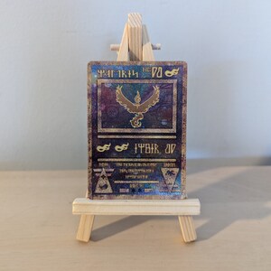 Pode incluir: Um cart&atilde;o Pokemon dourado e azul com uma imagem hologr&aacute;fica do Pokemon Moltres. O cart&atilde;o est&aacute; em um pequeno cavalete de madeira.