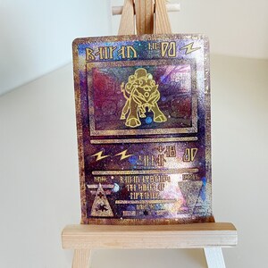 May include: A gold and purple holographic Pokemon card featuring a golden Raichu with the text "Raichu No. 26 Zz", "Lightning" symbol, and "Level 18 07" in the background.