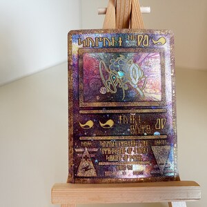 May include: A holographic trading card with a gold and purple background. The card features a holographic image of a creature with a blue eye. The card text reads "DARK" and "ATK 2000 DEF 2000".