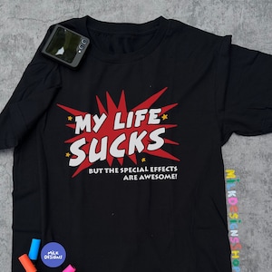 May include: Black t-shirt with a red and white graphic that says "My Life Sucks But The Special Effects Are Awesome!"