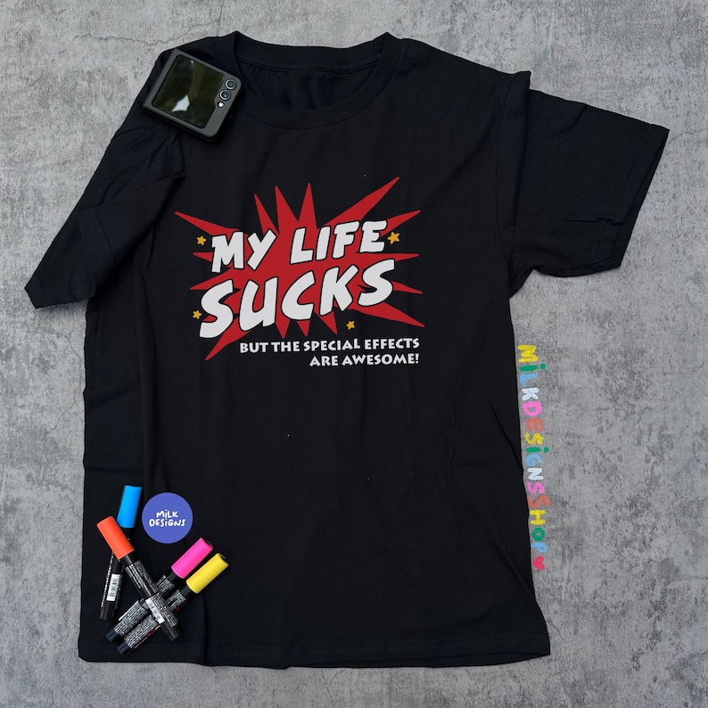 May include: Black t-shirt with a red and white graphic that says "My Life Sucks But The Special Effects Are Awesome!"