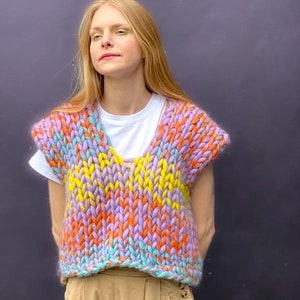 May include: A sleeveless knitted vest with a chunky knit texture in a rainbow color pattern of purple, yellow, orange, and blue.