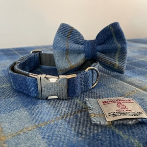 May include: A blue plaid dog collar and matching bow tie set. The collar has a silver metal buckle and a gray nylon strap. The bow tie is pre-tied. A Harris Tweed label is also visible.