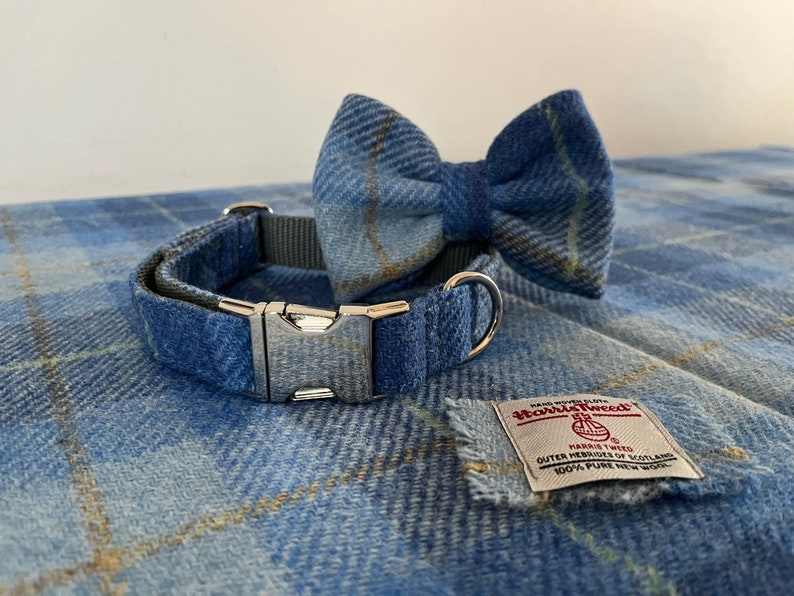 May include: A blue plaid dog collar and matching bow tie set. The collar has a silver metal buckle and a gray nylon strap. The bow tie is pre-tied. A Harris Tweed label is also visible.