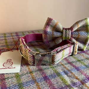 May include: A dog collar and matching bow tie set in a colorful plaid pattern. The collar has a pink interior and a silver buckle. A white tag with the Harris Tweed logo is attached.