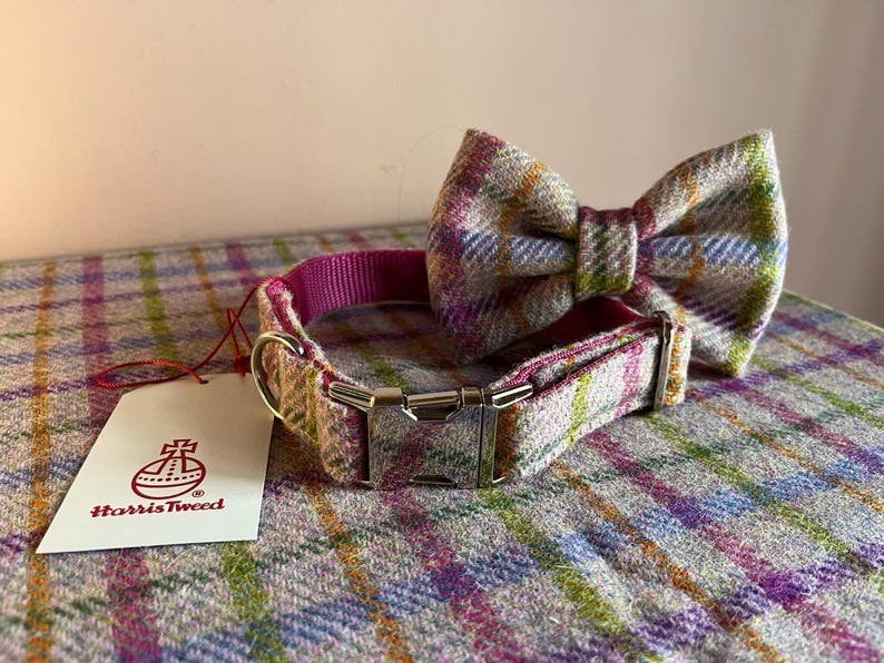 May include: A dog collar and matching bow tie set in a colorful plaid pattern. The collar has a pink interior and a silver buckle. A white tag with the Harris Tweed logo is attached.
