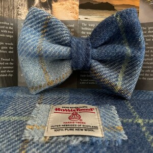 May include: A blue tweed bow tie with a matching fabric square. The bow tie is made of a textured fabric with a plaid pattern. A label on the fabric square reads "Harris Tweed Outer Hebrides of Scotland 100% Pure New Wool."