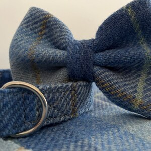 May include: Close-up of a blue denim dog collar with a matching bow tie. The collar has a silver metal ring. The bow tie and collar are made of a blue denim fabric with a subtle plaid pattern in yellow and green.