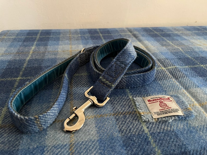 May include: A blue plaid dog leash with a silver metal clasp and a matching blue plaid fabric. The leash has a teal lining and a Harris Tweed label.