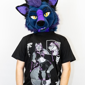 Może przedstawiać: Osoba nosząca niebiesko-fioletową głowę fursuit wilka i czarny t-shirt. T-shirt przedstawia grafikę wilka w bluzie z kapturem i napis "AL'HER'S CREATIVE DUNGEON". Fursuit ma żółte oczy.