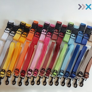 Pode incluir: Vinte e duas correias coloridas com fivelas e clipes pretos. As correias estão dispostas em duas filas, com as fivelas e os clipes virados para cima. As correias são feitas de uma variedade de materiais, incluindo nylon, algodão e couro. As correias são de diferentes cores, incluindo vermelho, laranja, amarelo, verde, azul, roxo e marrom.