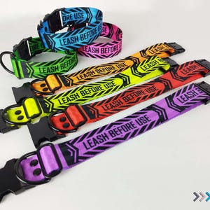 May include: Six colorful dog collars with black metal hardware and the text "LEASH BEFORE USE" printed on them. The collars are in the colors purple, black, orange, yellow, green, and blue.