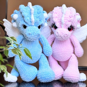 May include: Two crocheted plush dragon toys, one blue and one pink, with white wings and eyes.